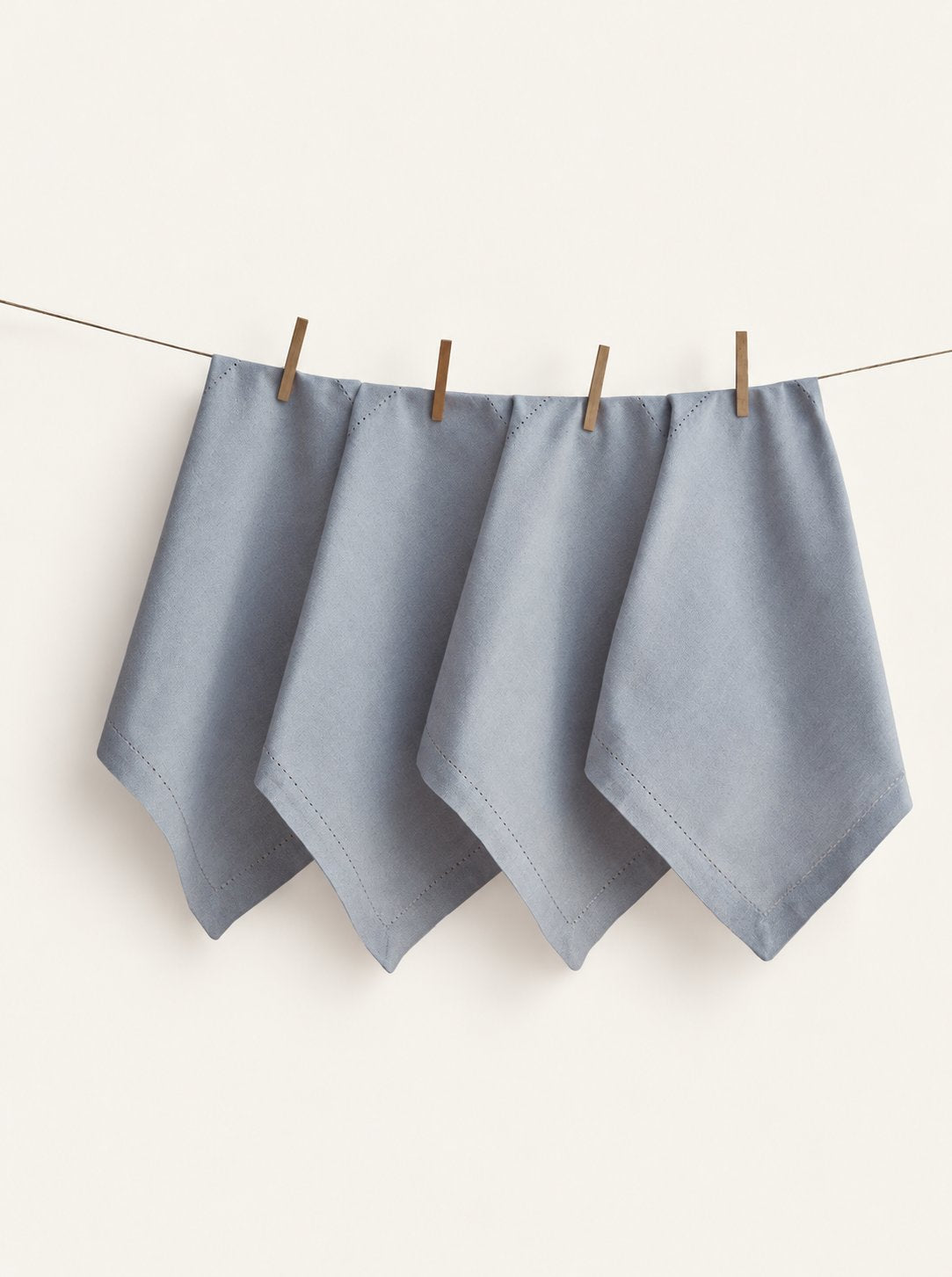 Four Jolly Light Grey napkins with hemstitched borders, displayed on a line with wooden pegs