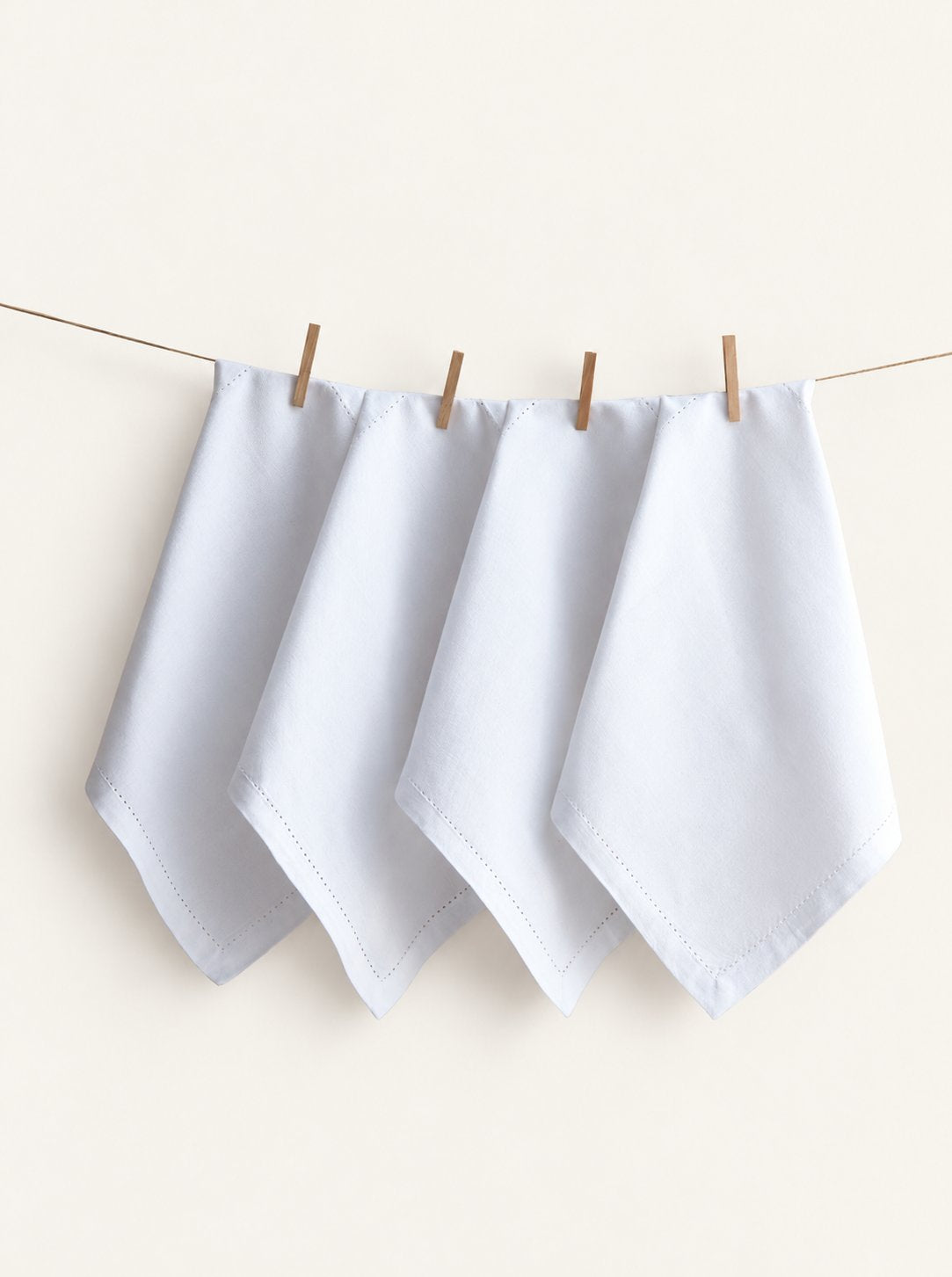 Four Jolly White napkins with hemstitched borders, displayed on a line with wooden pegs