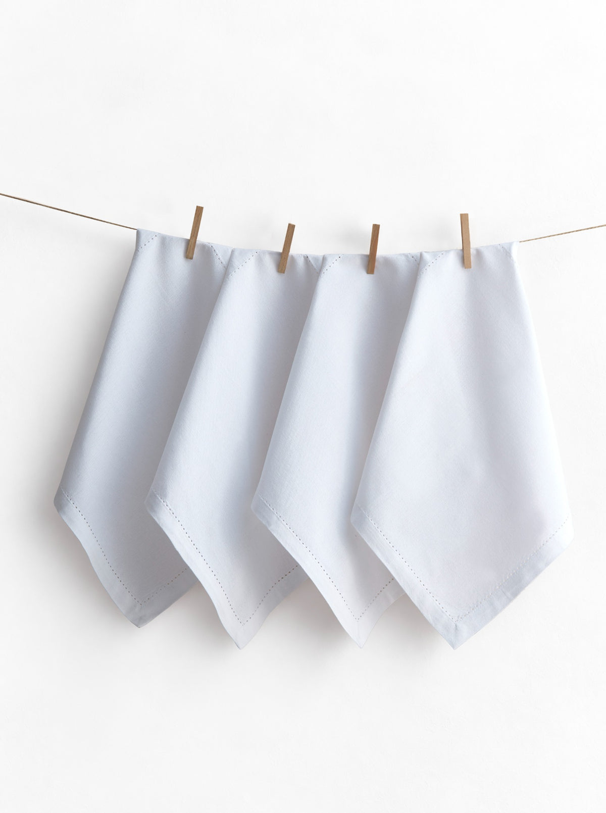 Four Jolly White napkins with hemstitched borders, displayed on a line with wooden pegs