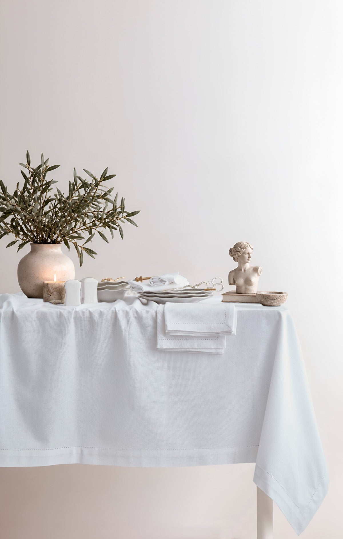 Jolly White tablecloth styled on a dining table with candles and an olive branch