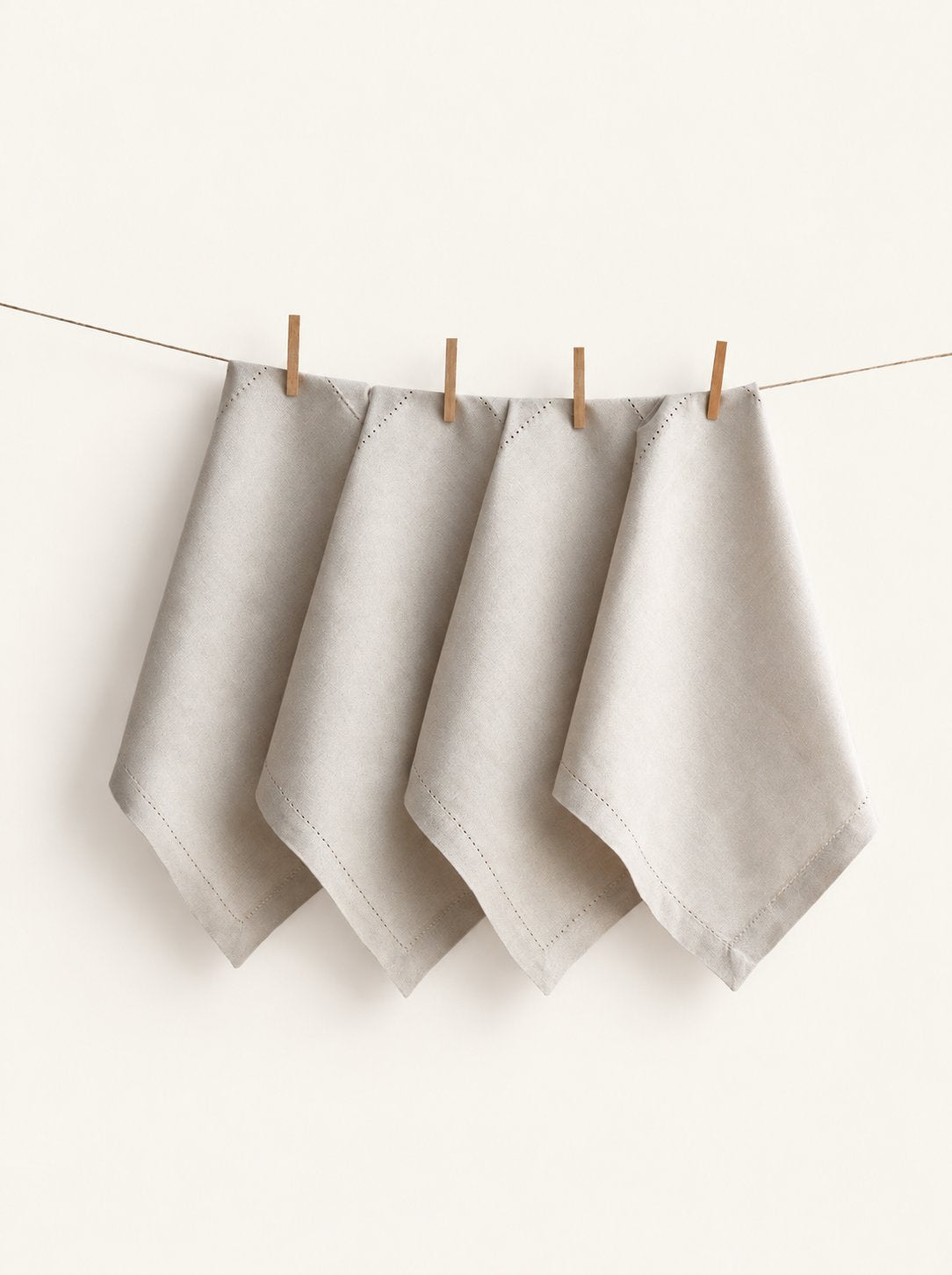 Four Jolly Light Beige napkins with hemstitched borders, displayed on a line with wooden pegs