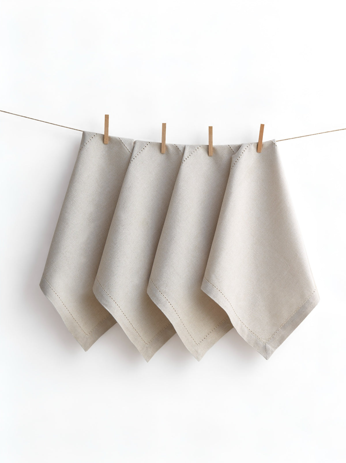 Four Jolly Light Beige napkins with hemstitched borders, displayed on a line with wooden pegs