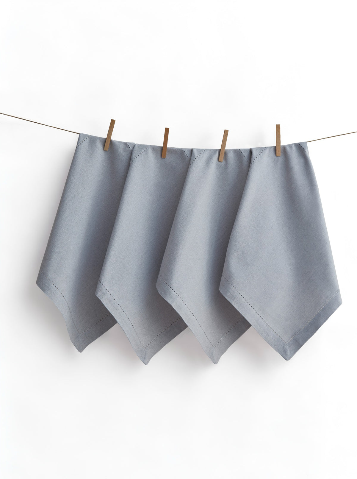 Four Jolly Light Grey napkins with hemstitched borders, displayed on a line with wooden pegs