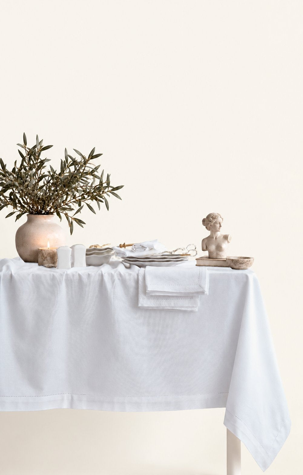 Jolly White tablecloth styled on a dining table with candles and an olive branch