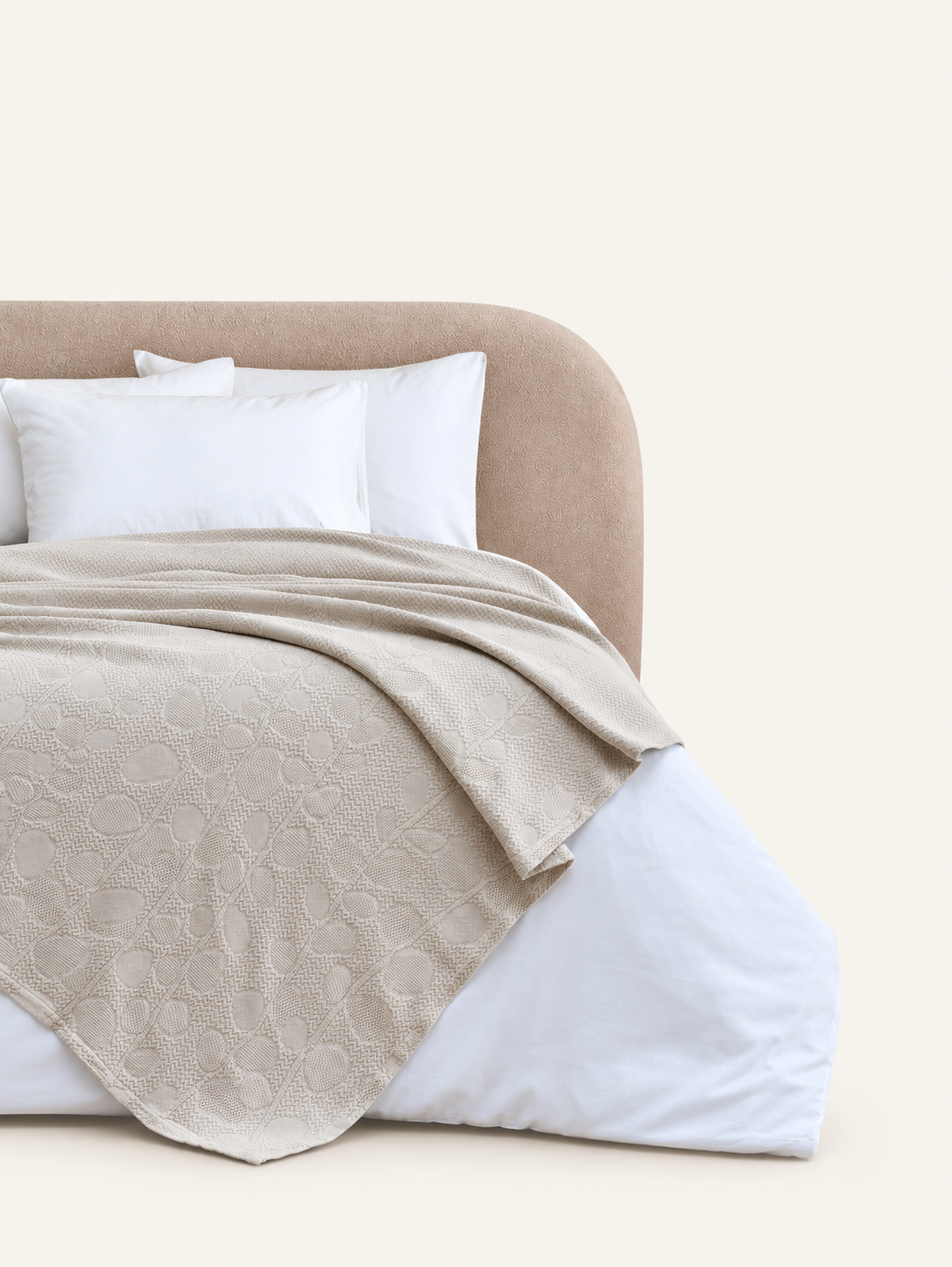 Solena beige throw with leaf motifs displayed on a bed against a light beige background